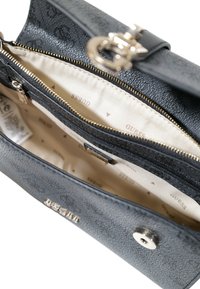 Schwarze synthetische Handtasche mit strukturiertem Äußeren, goldenen Reißverschlüssen und einem beigen Innenraum mit einem bedruckten Logo-Design. Enthält eine Reißverschlusstasche.