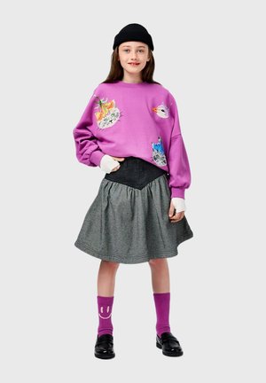 Felpa viola con design di gatti, gonna svasata grigia, stivali neri e calzini viola con faccina sorridente. Outfit accogliente e informale.