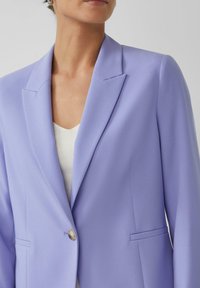 Lavendel blazer met een notched lapel, enkele knoopsluiting en twee frontzakken. Gladde stoftextuur en een getailleerde pasvorm.