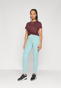 Burgunderfarbendes geknotetes T-Shirt, kombiniert mit hellblauen Leggings und schwarzen Sportschuhen mit weißen Akzenten. Glattes, angepasstes Design.