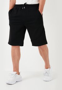 Pantaloni neri corti realizzati in un tessuto morbido, con vita elastica e cordoncino, tasche laterali e lunghezza fino al ginocchio.