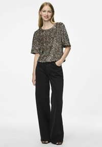 Top de lentejuelas en tonos bronce con mangas cortas y un ajuste relajado, combinado con jeans de pierna ancha de talle alto en negro y zapatos negros de punta abierta.