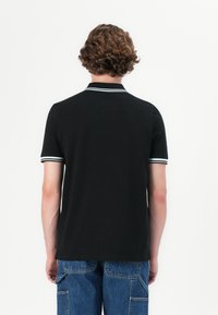 Black polo shirt with a collar and two white stripes at the neckline and sleeves. Short sleeves and straight hem, made of smooth fabric.
