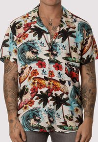 Camisa de manga corta con botones que presenta un colorido estampado tropical con perros, flores y tablas de surf sobre un fondo blanco.