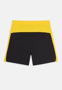 Svarte treningsshorts med en gul toppdel. Har en elastisk midje og sidepaneler i kontrastfarger. Glatt tekstur.