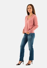 Maglione rosa a V con maniche lunghe, abbinato a jeans dritti blu e sandali neri con tacco alto. Design semplice, texture liscia.