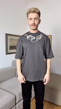 T-shirt cinza de manga curta com um gráfico de cobra branca no peito. O tecido parece suave e o ajuste é descontraído.