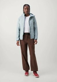 Ανοιχτό μπλε επενδυμένο μπουφάν με κουκούλα, λευκό μπλουζάκι, καφέ χαλαρές παντελόνες και κόκκινα παπούτσια πεζοπορίας. Ορατές πλαϊνές τσέπες στις παντελόνες.