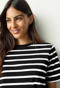 Črno-bela majica na črte s kratkimi rokavi in okroglim izrezom. Tkanina je videti mehka z gladko teksturo.
