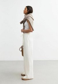Pantalones anchos blancos de pierna ancha con cintura elástica, combinados con una camiseta ceñida blanca y un suéter marrón claro caído sobre los hombros.