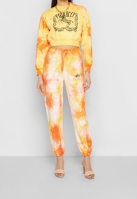 Geel en oranje tie-dye sweatshirt en joggers met logodetails. Zacht materiaal, aansluitend ontwerp, elastische boorden en tailleband. Huidskleurige hoge hakken.