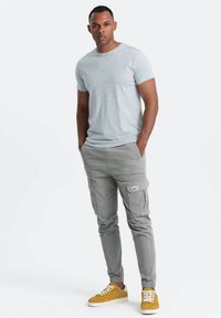 Lys grå kortærmet t-shirt, letgrå cargo-bukser med sidelommer og gule sneakers med hvide snørebånd. Glat tekstur, afslappet pasform.