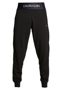 Zwarte joggers met een dikke, gemerkte tailleband. Gemaakt van zachte stof met zijzakken en elastische boorden bij de enkels.