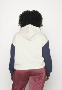 Felpa con cappuccio caratterizzata da un corpo crema e maniche blu navy, realizzata in tessuto morbido, che offre una vestibilità comoda e una tasca a marsupio.