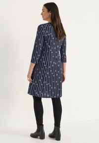 Mekko tummansinisellä pohjalla, joissa on rohkeat mustat pystysuorat raidat, kolmanneksen pituiset hihat, yhdistetty mustiin legginsseihin ja nilkkasaappaisiin. Tasainen pinta.