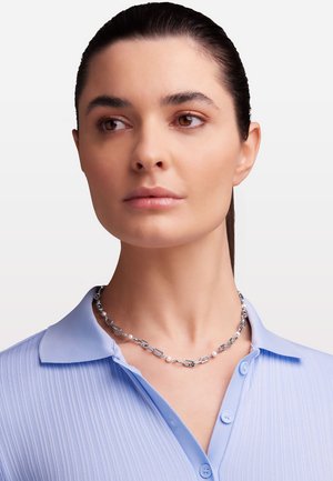 Silberne Kettenhalskette mit ovalen Gliedern und kleinen Perlen, getragen über einem hellblauen Hemd mit Kragen aus strukturierter Stoff.