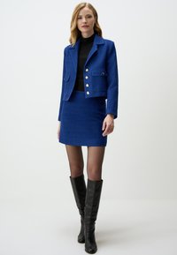 Blue textured fabric blazer with large buttons, paired with a matching skirt and black knee-high boots. Features a tailored design.