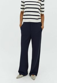 Navy wide-leg trousers made from a smooth fabric, paired with a striped short-sleeve top. The model wears pointed shoes with a striped pattern.
