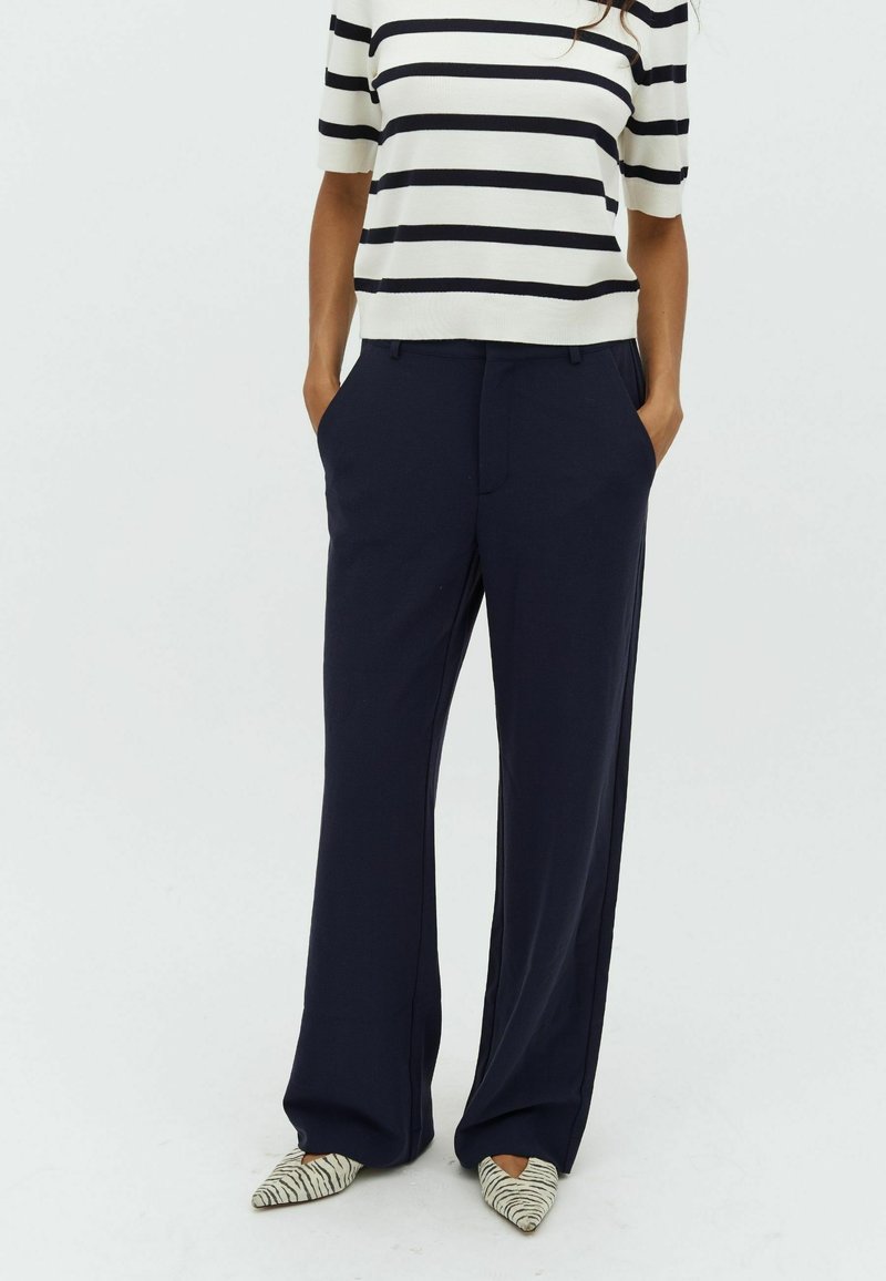 Navy wide-leg trousers made from a smooth fabric, paired with a striped short-sleeve top. The model wears pointed shoes with a striped pattern.