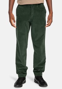 Green corduroy pants with a straight-leg design, featuring front pockets and a button closure. Smooth texture, paired with black shoes.