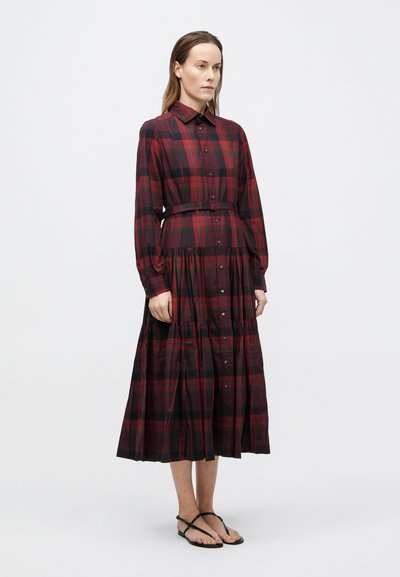 Tumši sarkana plāno kokvilnas kleita ar garām piedurknēm, rūtainu rakstu, pieguļošu vidukli un slāņveida svārkiem.