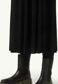 Black pleated skirt paired with black leather ankle boots featuring elastic side panels and a chunky sole. The skirt displays fine vertical stripes.