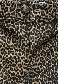 Pantalon à imprimé léopard en jean beige et noir. Comprend une fermeture à glissière et un bouton métallique, avec un tissu texturé et des surpiqûres contrastantes.