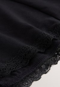Tissu noir avec une délicate bordure en dentelle florale le long du bord, montrant la texture et les détails fins de couture.