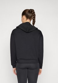 Svart hettegenser med ribbestrikket nederkant og mansjetter, laget av mykt stoff. Har en avslappet passform og bakvisning, stylet med matchende svarte leggings.