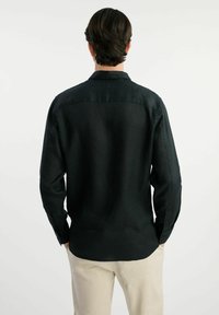 Czarna lniana koszula z długimi rękawami i mankietami na jeden guzik, o prostym kroju i karczku z tyłu, umieszczona na jasnym tle.