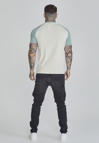 Short-sleeve, cream t-shirt with light blue raglan sleeves. Black cargo pants with pockets. White sneakers. Clear tattoos on arms and neck.