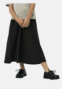 Jupe noire longueur cheville avec une texture lisse, associée à des chaussures noires à lacets avec une semelle épaisse. T-shirt gris décontracté au-dessus.