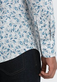 Lichte katoenen shirt met een witte basis, voorzien van een blauw loofpatroon. De mouw is knoopsgat en het is gecombineerd met donkerdenim jeans.