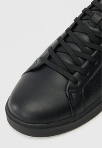 Tenis din piele neagră cu un finisaj neted, având șireturi negre plate, accente perforate și o talpă robustă din cauciuc.