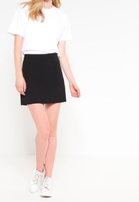 Svart kjol med åtsittande midja och två fickor, ihopparad med en vit t-shirt och vita sneakers. Slät textur och klassisk design.