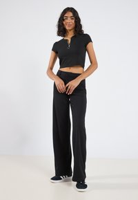 Musthave musta riidebändiga lühikesed varrukad crop top, millel on tõmbluku sulgemine, kombineeritud kõrge vöökoha mustade laia säärega pükstega ja mustade tossudega, millel on valged aktsendid.