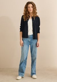 Cardigan blu navy con bottoni, abbinato a un top bianco e jeans a gamba larga azzurri. Sneakers casual completano l'outfit. Materiale testurizzato.