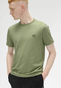 T-shirt a maniche corte color verde oliva realizzato in tessuto liscio, con un piccolo logo ricamato di colore verde scuro sul petto.