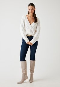 Hvid strikket sweater med dyb V-hals, strukturerede mønstre, mørkeblå skinny jeans og lys grå knæ-høje spidse støvler med lynlåse.