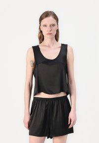 Svart, kort tanktop i glatt stoff, kombinert med svarte elastiske shorts med liv. Begge plaggene har et enkelt, minimalistisk design.