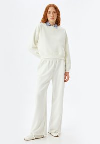 Witte sweatshirt en broek set, met een zachte textuur, wijde broekspijpen en ribgebreide manchetten, gecombineerd met een lichtblauwe gestreepte overhemd met kraag eronder.