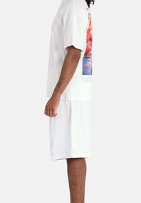 T-shirt oversize blanche avec un graphique coloré sur le devant, associé à un short blanc. Le tissu semble doux, au design décontracté.