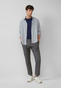Svijetlosiva košulja na kopčanje preko tamnoplavog majice, u kombinaciji sa sivim slim-fit hlačama i bijelim tenisicama s teksturiranim detaljima.