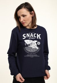 Mörkblå sweatshirt med långa ärmar som har en vit hajgrafik och texten "SNACK ATTACK" på framsidan. Tillverkad av bomull, avslappnad passform.