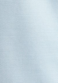 Gros plan d’un tissu bleu tissé avec un petit motif diagonal en tissage panier répétitif et des ombres douces.