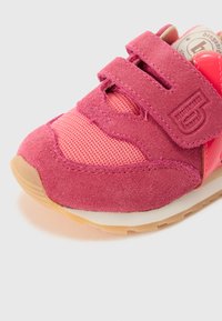 Pink athletic shoe featuring a combination of suede and mesh materials, with a textured surface, Velcro strap, and rubber sole.