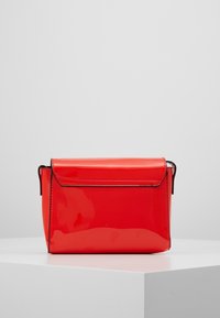 Rød, blank, rektangulær håndtaske med klaplukning, præsenteret på en hvid pedestal mod en neutral baggrund.