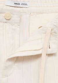 Lněné kalhoty v bílé barvě s jemnými vertikálními pruhy. Mají přední zapínání na knoflík a vnitřní stahovací šňůrku. Měkká textura.