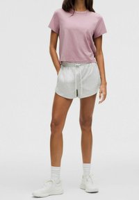 Světle růžové bavlněné tričko s krátkým rukávem, spárované se šedými šortkami na stahovací šňůrku. Model má na sobě bílé tenisky a pruhované ponožky.
