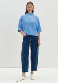 Blauer gerippter Strickpullover mit hohem Kragen, kombiniert mit hochtaillierten dunklen Jeans und weißen Turnschuhen. Einfaches Design, lockere Passform.